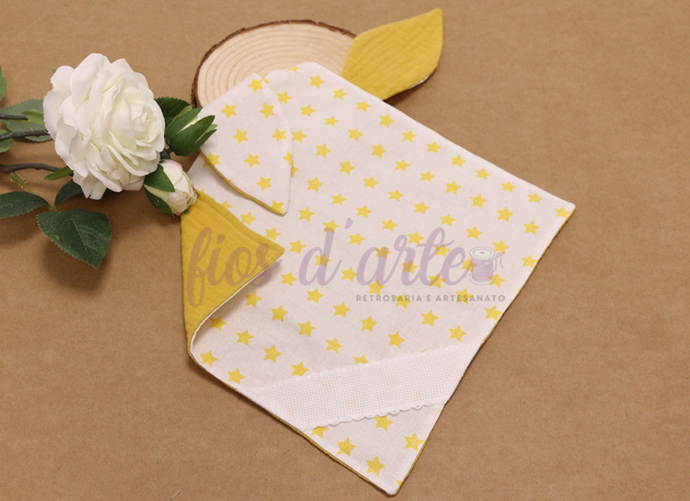 Toalha de bebé amarela e branca com padrão de estrelas e flor branca ao lado