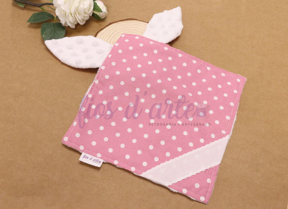 Doudou/ Naninha Orelhinhas para bordar ponto cruz #10 (Fios d'arte) Lenço rosa com pintas brancas e orelhas brancas texturizadas sobre superfície castanha com flor e madeira