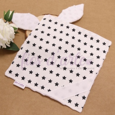 Toalha de rosto branca com estrelas pretas e orelhas pontudas sobre superfície castanha ao lado de flor branca