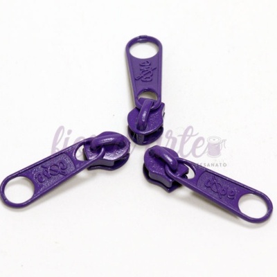 Três puxadores de zíper roxos, metálicos, sobre fundo branco.