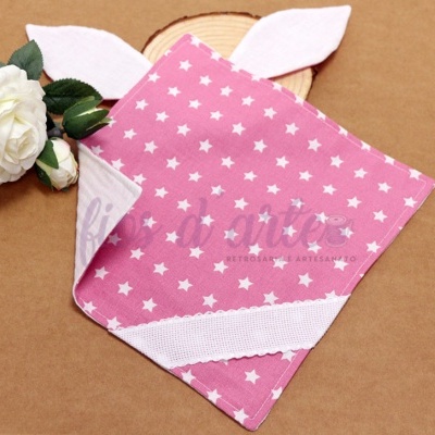 Toalha rosa com estrelas brancas e detalhes em branco, com orelhas, junto a flores brancas e folhas verdes.