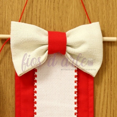 Laço artesanal vermelho e branco pendurado em suporte de madeira