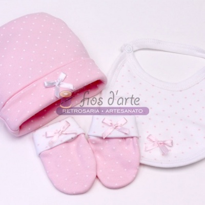 Conjunto de bebé rosa e branco com gorro, luvas e babete.