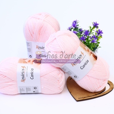 Três novelos de lã rosa clara com etiquetas da marca Rosári e flores roxas ao fundo