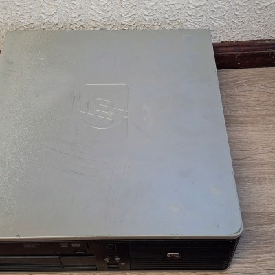 Computador desktop compacto HP cinza sobre mesa de madeira