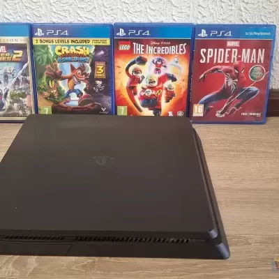 Consola PS4 preta com quatro jogos PlayStation 4 atrás em chão de madeira.