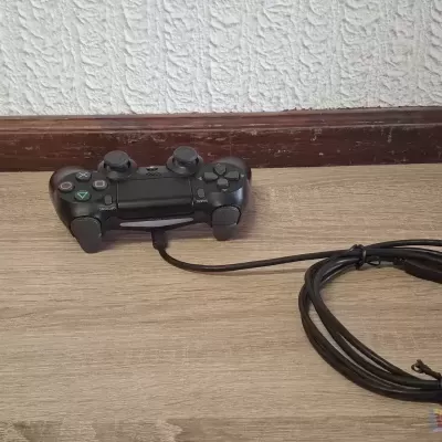 Comando videojogo preto com cabo em chão de madeira e parede branca