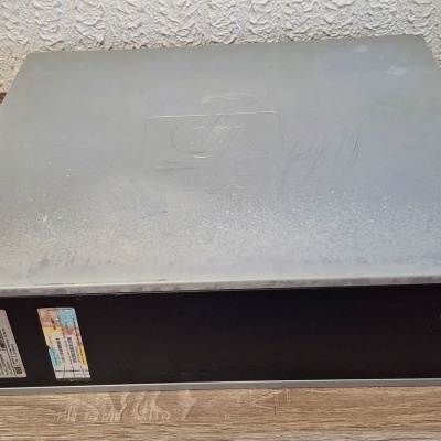 Computador desktop cinza com frente preta em chão de madeira clara junto a parede branca