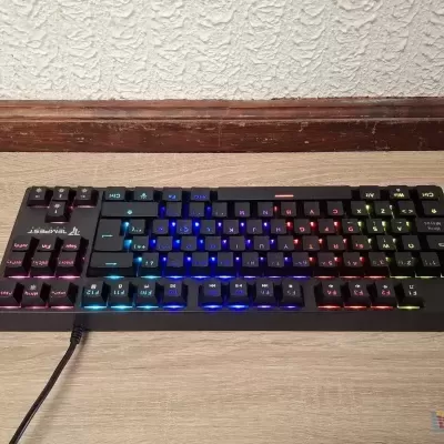 Teclado mecânico preto com iluminação LED colorida sobre superfície de madeira clara.