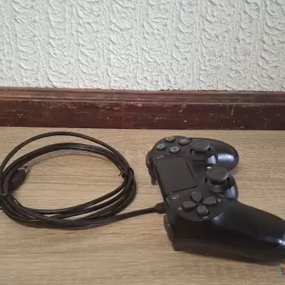 Comando de videojogo preto com cabo no chão de madeira junto a parede.