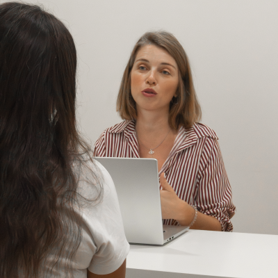 Duas mulheres numa mesa, uma com laptop prateado.