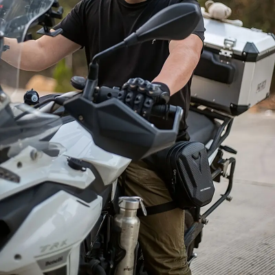 Motocicleta branca TRK com malas e bolsa preta, condutor com luvas e roupa casual em ambiente exterior.