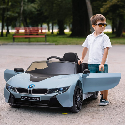 Carro elétrico infantil BMW i8 COUPE azul claro com menino ao lado num parque