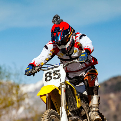 Motociclista com capacete vermelho e preto, roupa branca com detalhes vermelhos e amarelos, luvas azuis e botas castanhas numa moto amarela com número 85