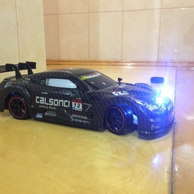 Carro de corrida rádio controlado preto com farol ligado e adesivos CALSONIC e número 12