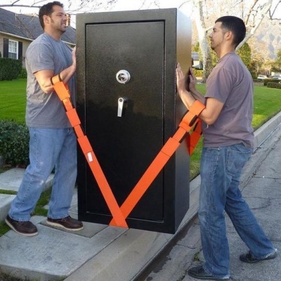 Dois homens a transportar um cofre preto com cintos laranja na rua