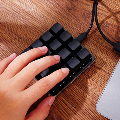 Teclado numérico compacto preto sobre mesa de madeira com mão esquerda a tocar.