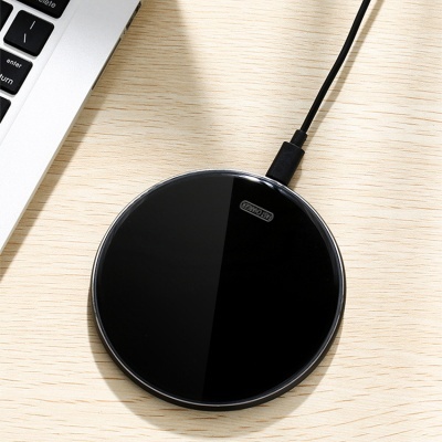 Carregador sem fios preto redondo com cabo USB ao lado de portátil