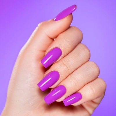 Mão com unhas roxas brilhantes em fundo roxo