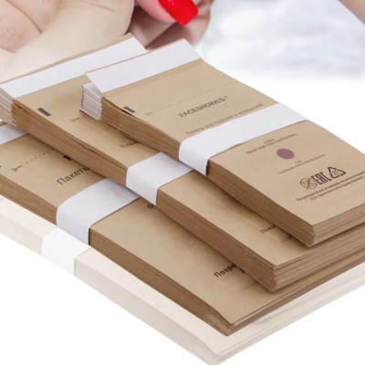 Conjuntos de pads de lixa para unhas em embalagem de papel kraft com faixa branca e mão com unhas vermelhas ao fundo.