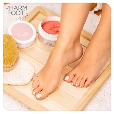 Pés femininos com creme esfoliante Pharm Foot e escova sobre bandeja de madeira