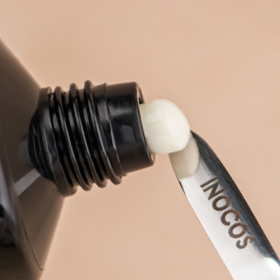 Tubo preto de creme com creme branco e espátula metálica com palavra INOCOS