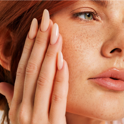 Close-up rosto mulher ruiva com unhas artificiais nude brilhante