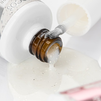 Frasco de vidro castanho com líquido viscoso branco a escorrer e aplicador branco