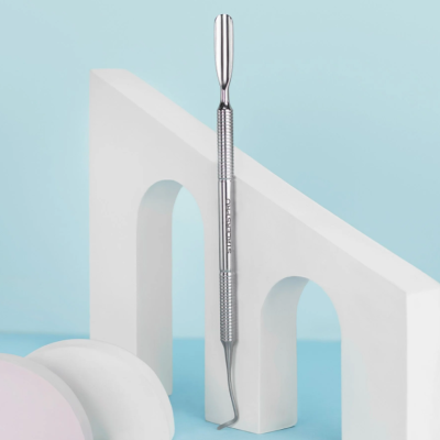 Instrumento metálico para cuidado dental com duas pontas, sobre estrutura branca com arcos, fundo azul claro