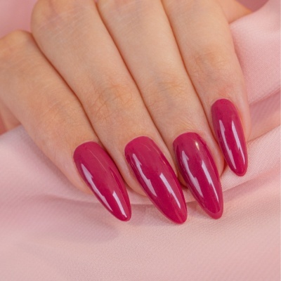 Unhas artificiais compridas com verniz vinho brilhante sobre tecido cor de rosa