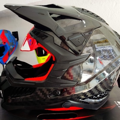 Capacete integral preto com fibra de carbono sobre caixa LS2 com capacetes coloridos ao fundo