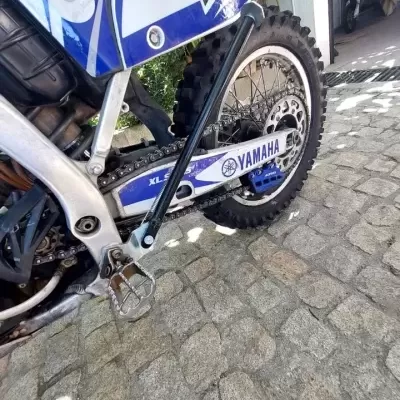 Mota motocross Yamaha azul e branca com pneus de cravos e placa lateral com texto