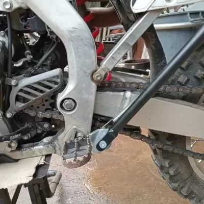 Detalhe da estrutura, pedal e correia de uma moto todo-terreno com pneu cravado e mola de suspensão vermelha