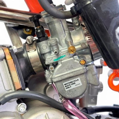 Carburador metálico prateado com parafusos dourados e tubos em borracha preta num motor