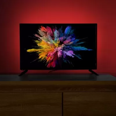 Televisor com imagem colorida sobre móvel de madeira e fundo vermelho