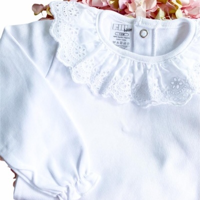 Camisola branca de bebé com gola rendada sobre flores artificiais