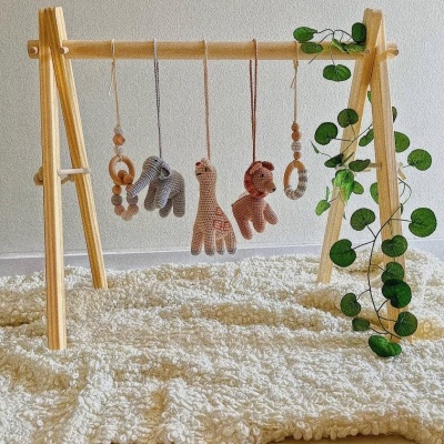 Ginásio de bebé de madeira clara com penduricalhos tricotados e planta verde