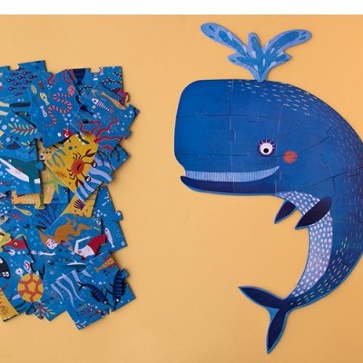 Puzzle desmontado e molde em formato de baleia azul sobre fundo laranja