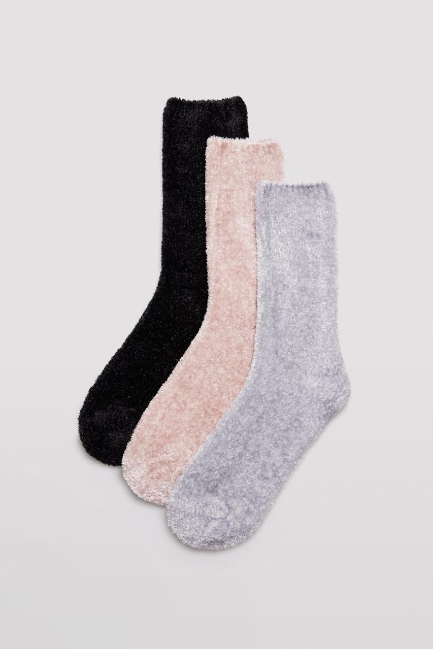 Três pares de meias felpudas em preto, rosa claro e cinza sobre fundo cinza