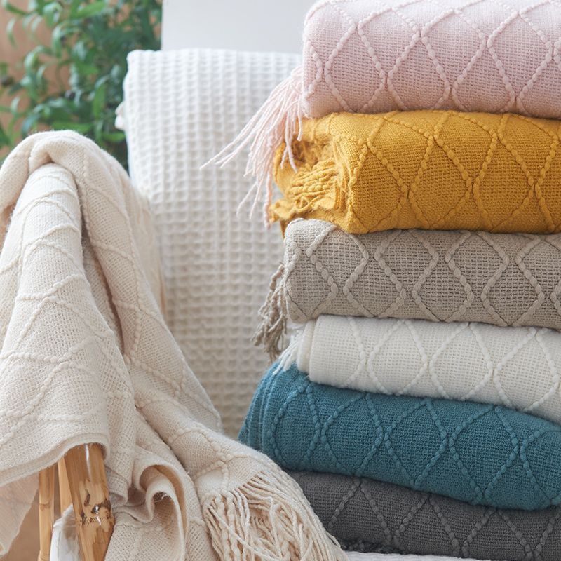 Opal Mantas de malha coloridas com padrão em losangos empilhadas em sofá branco junto a planta