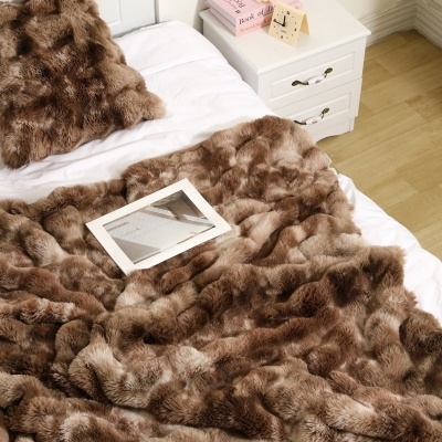 Manta e almofada de pelo castanho em cama branca ao lado de mesa de cabeceira e chão de madeira clara