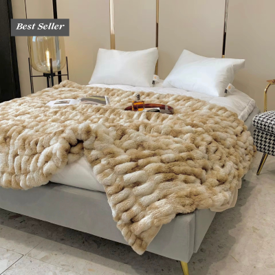 Manta felpuda bege sobre cama cinza com almofadas brancas e candeeiro de pé