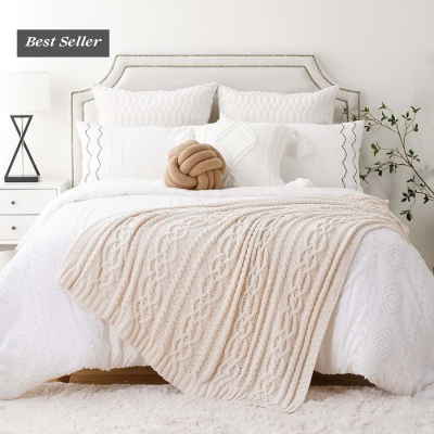 Cama com cabeceira branca, roupa de cama branca, manta bege de malha e almofadas decorativas