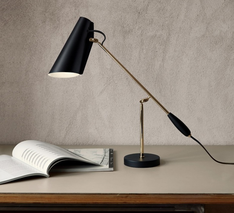 Candeeiro de mesa preto e dourado numa mesa com livro aberto e parede cinza de fundo