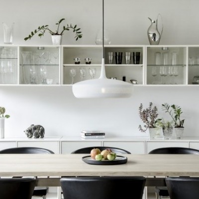 Sala de jantar com mesa de madeira, cadeiras pretas e prateleira branca com copos e jarros