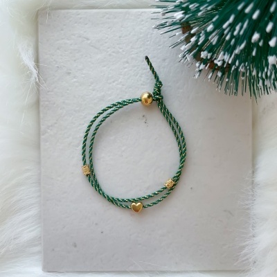 Pulseira verde com detalhes dourados sobre base branca texturada e fundo peludo