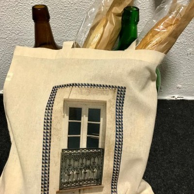 Saco de tecido bege com estampa de janela, garrafas de vidro e baguetes embaladas