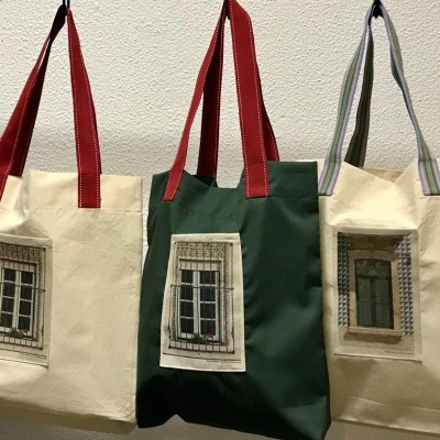 Três sacos de tecido com estampas de janelas, pendurados numa parede branca.