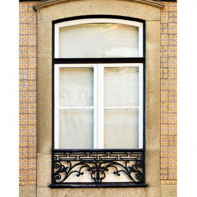 Janela com aro em pedra e grade preta embutida em parede com azulejos coloridos