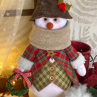 Boneco de neve decorativo vestido com casaco xadrez e chapéu castanho segurando coroa pequena verde e vermelha